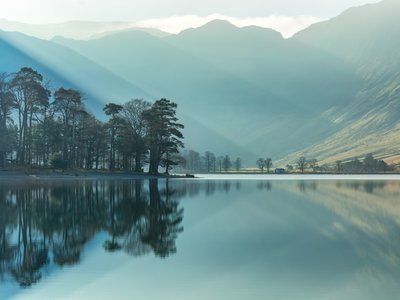 Misty morning with calm reflections of tree's in lake at Buttermere, Lake District, Cumbria, UK