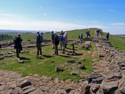 Ramble Worldwide walking group on Hadrian's Wall exploring stone ruins in grassy hill countryside of Northumberland