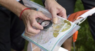 Hand holding compass on map to navigate route using orienteering skills