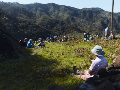 Behind shot of walker enjoying quiet lunch whilst sat down away from group taking in the view of the mountains, Tenerife, Spain