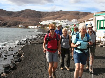 Ramble Worldwide walking group walking along black sand beach arriving at Playa Quemada village, Lanzarote, Spain