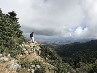 Person standing atop rocky cliff edge taking in view of mountainous landscape of Sierra de las Nieves on cloudy and sunny day, Sierra de las Nieves, Andalucia, Spain