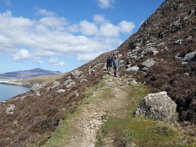 Two people descending mountainside dirt pathway with blue sea and sky in frame, The Outer Hebrides, Scotland