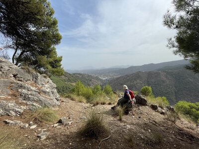 Hiker sat on rock on mountain starring off into distance absorbing view of mountain range in Sierra de las Nieves, Spain