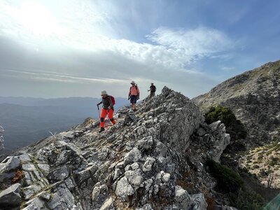 Three hikers traversing over jagged rocks high up in mountains on sunny day, Sierra de las Nieves, Andalucia, Spain