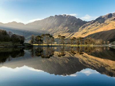 Calm waters of Buttermere Lake reflecting Haystacks fell towering from behind with sun shining through blue skies, Lake District, England