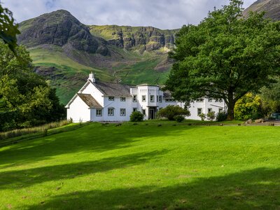 Hassness House and front garden with grass field and oak trees, Robinson Fell behind