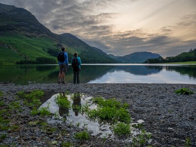 Male and female walkers on Ramble Worldwide walking holiday standing at edge of Buttermere Lake taking in view of Lake District