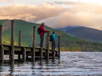 Two people on a Ramble Worldwide walking holiday standing on wooden dock at Derwentwater in Lake District during sunrise