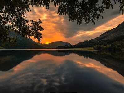View from Crummock Water shore of sun setting behind Lake District fells with reflection