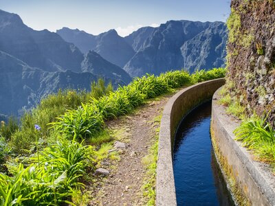 View from Levada do Norte with irrigation canal bending around mountain path and green mountains in background, Madeira, Portugal