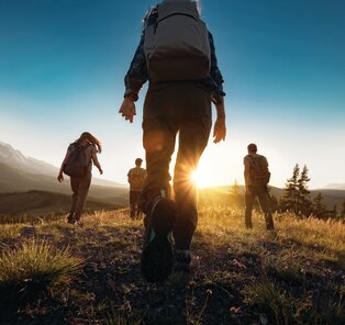 Group walking on grassy field moving towards sun on a walking holiday