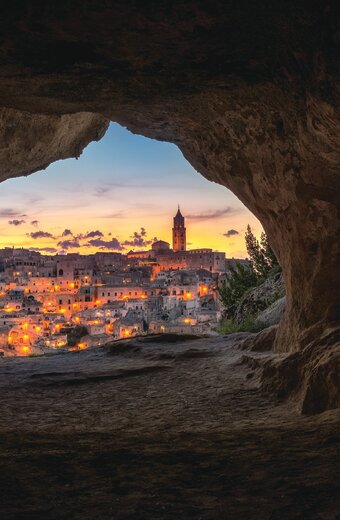 Cave in Matera with view of city at dusk and orange light glow, Italy
