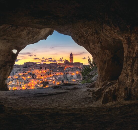 Cave in Matera with view of city at dusk and orange light glow, Italy