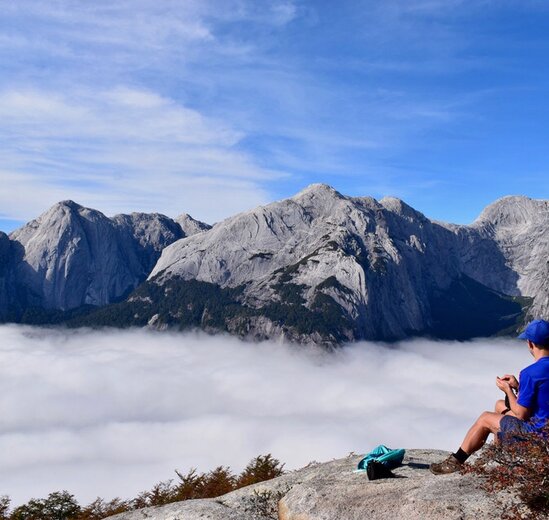 Solo traveller sitting taking in view of Cochamo Valley, Chile on a walking holiday