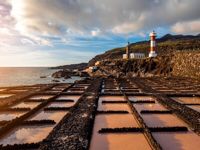 Coastal view of Faro de Fuencaliente lighthouse and salt manufacturing pools with mountains in background on sunny day, La Palma, Spain