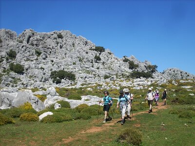 Walkers traversing down grasshill with rocky mountain in background, Grazalema, Spain