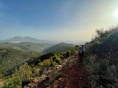 Mountainous landscape with line of hikers following dirt path towards camera, Sierra de las Nieves, Andalucia, Spain