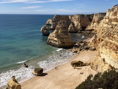 Coast of Western Algarve showing tall cliffs and rock formations with gentle waves crashing into sandy beach, Portugal