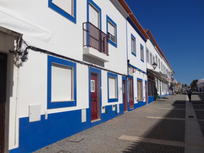 Facade of white Portuguese houses and royal blue painted outline in street with clear blue skies on sunny day, Portugal