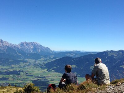 Couple of hikers sat on grass near walking trail admiring landscape of Maria Alm in Austria