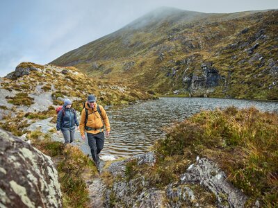 Man and woman walking past a mountain lake in outdoor clothing