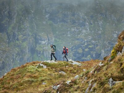 Man and a woman walking on a dramatic ridge in the mountains in outdoor clothing