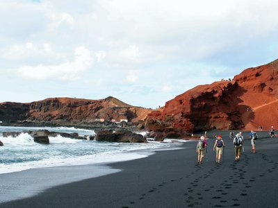 Small walking group walking along black sand beach at El Golfo, Lanzarote, Spain, Europe