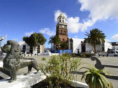 Lion statue in foreground with background showing Church Iglesia de Nuestra Senora de Guadalupe on Plaza de la Constitucion, Teguise, Lanzarote, Canary Island, Spain