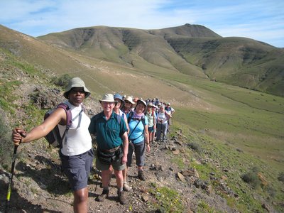 Line of walkers pausing during ascent to smile for picture with faint grassy mountainous landscape in background, Lanzarote, Spain