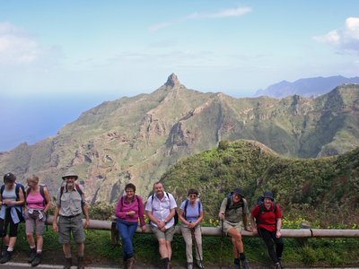 Group of walkers resting on wooden post facing camera with mountains in background amidst blue sky, Tenerife, Spain