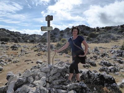 Female hiker proudly poised by Grazalema and mirador signpost on walking trail in Sierra de Grazalema on sunny day, Spain