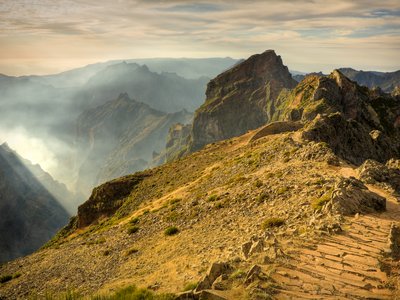 Golden glow from sunshine casting over the mountains of Pico Do Arieiro with clouds floating close by, Madeira, Portugal