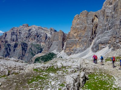 Group of walkers passing below a cliff face in the Dolomites, Italy, under bright blue skies 