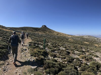 Three people walking in line on left towards hill in alpine tundra Sierra de las Nieves, Andalucia, Spain