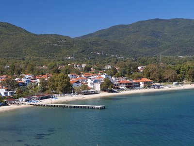 Coastal aerial view of Olympiada with green mountains in background under clear blue skies on sunny day, Greece